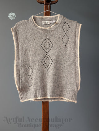 Knitted vest with diamond pattern on a wooden hanger against a gray background