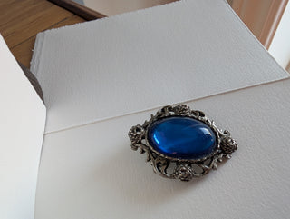 Transparent blue cabochon oval brooch with pewter-coloured floral frame