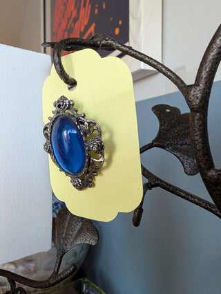 Transparent blue cabochon oval brooch with pewter-coloured floral frame